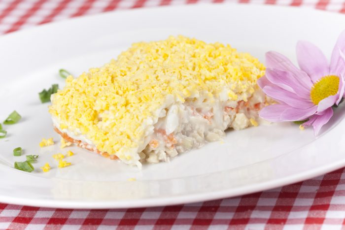 Салат мимоза на белой тарелке с цветком
