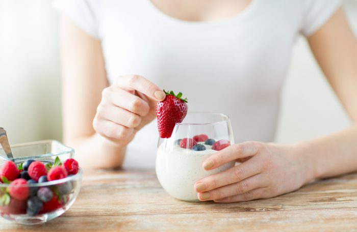 Девушка в белой майке держит йогурт с ягодами