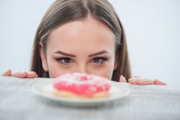 Девушка смотрит на пончик с розовой глазурью
