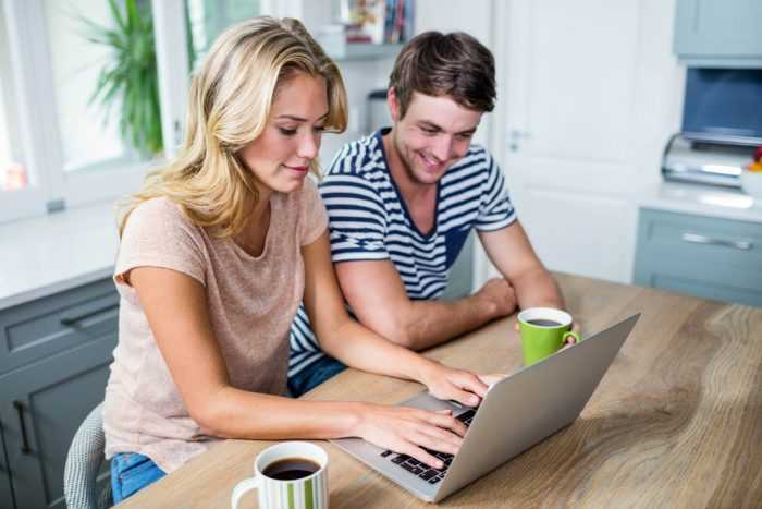 Парень с девушкой сидят за столом перед компьютером с чашками кофе