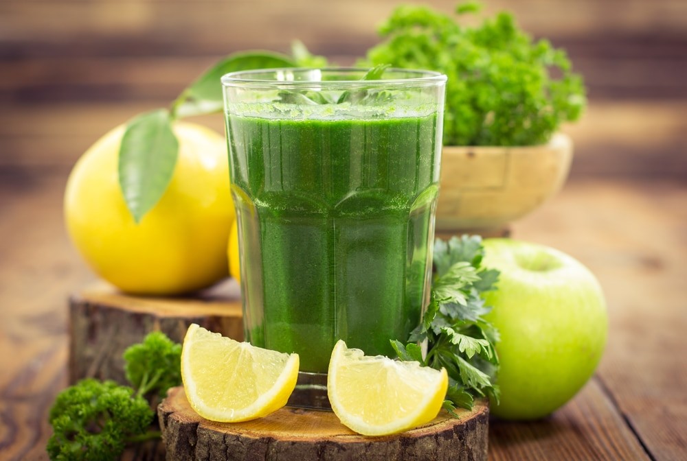 Зеленый сок в стакане возле зелени, лимона, яблока