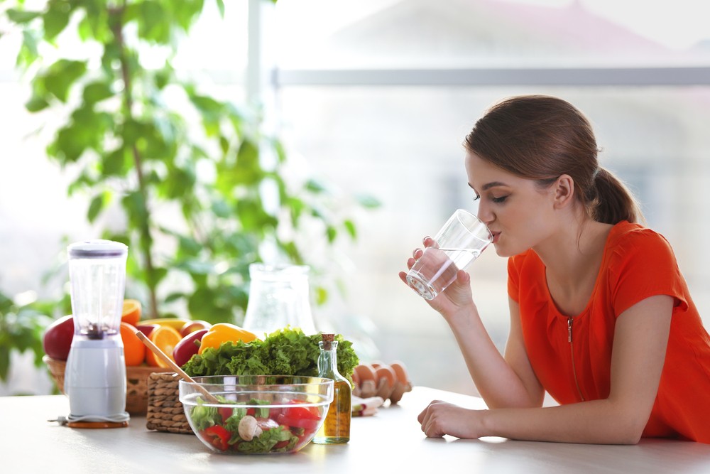 Девушка сидит за столом с салатом и пьет воду