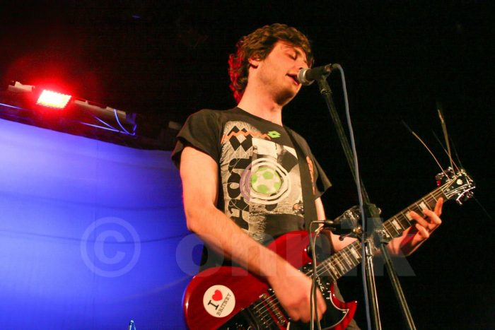 Ника Кочаров в черной футболке на сцене с гитарой
