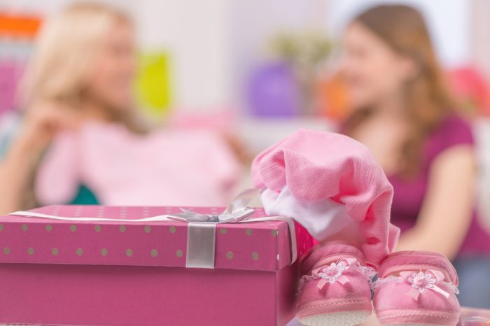На переднем плане подарочная розовая коробка и детские вещи