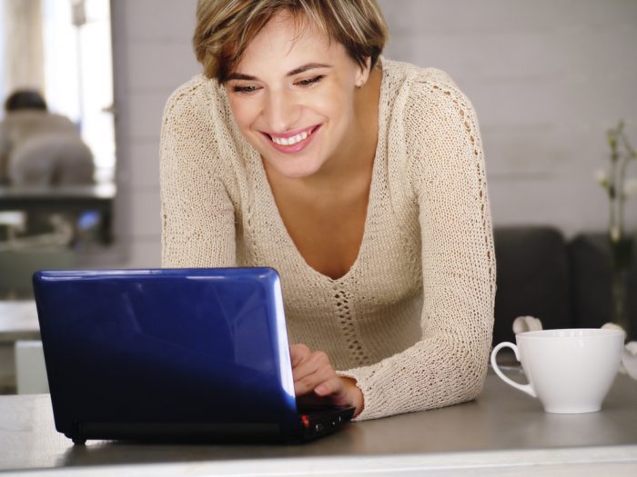 Женщина улыбается перед синим ноутбуком стоящим на столе с чашкой