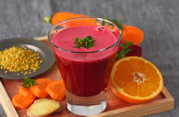 Свекольный сок в стакане возле порезанной морковки,апельсина